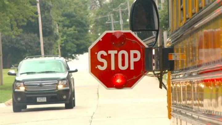 A car patiently waits for a school bus to let off students.