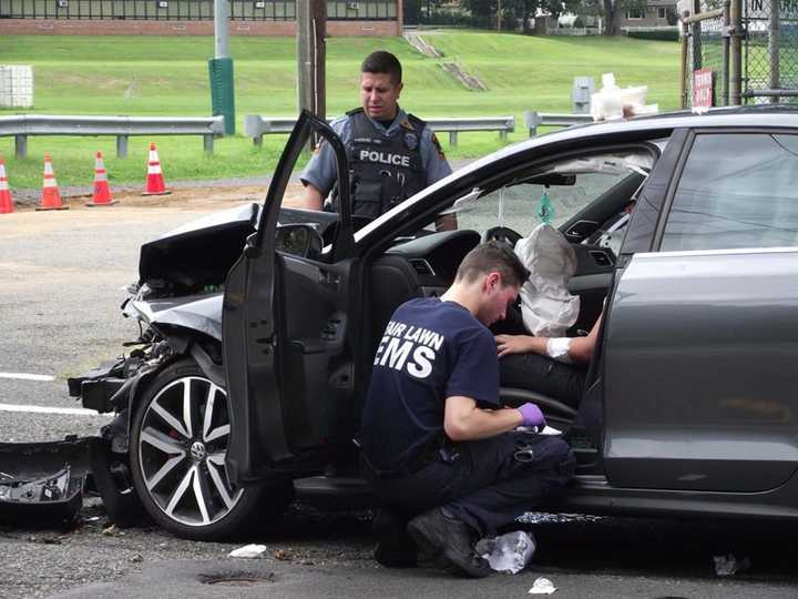 A Fair Lawn police officers surveys the damage to a vehicle involved in a Saturday crash, as EMS tends to the victim.