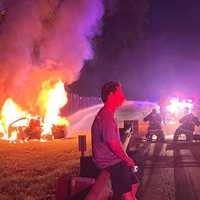 <p>Firefighters douse the flames on the Garden State Parkway moments before Jackson said the driver (seen talking with a New Jersey State Police trooper) suffered a seizure.</p>