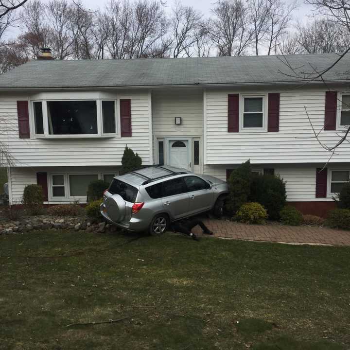 A tow truck driver works to remove a car from the front of the house it hit.