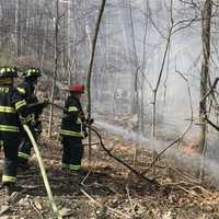 <p>Upper Saddle River firefighters douse a brush blaze following the crash on Lake Street on Sunday, March 19.</p>