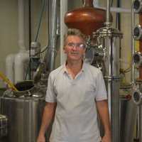 <p>Robert Schulten with some of the equipment used to make corn whiskey, gin and vodka at Asylum Distillery in Bridgeport.</p>