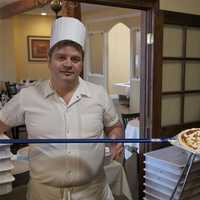 <p>Amore&#x27;s pizza chef shows off some of his work, pulling a pie from the restaurant&#x27;s hand made, Italian, wood-fired pizza oven.</p>