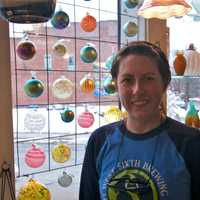 <p>Glass blower Kathleen Andersen in front of some of the store&#x27;s popular glass Christmas ornaments, which students can actually come in and make themselves.</p>