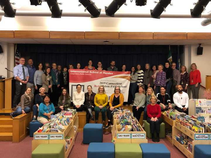 Greenwich Public Schools staff surround a banner presented to the staff and students at the International School of Dundee. The district received the 2019 Connecticut Red Ribbon PASS Program Award for its physical education program.