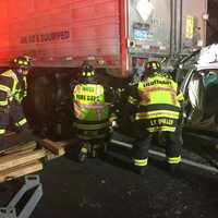 <p>Fairfield firefighters work at the scene of the multi-vehicle crash on I-95 early Tuesday. in which a car was lodged partially under a truck.</p>