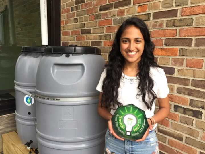 Greenlight Award Competition winner Rachel Joseph of Somers High School holding her Greenlight Award next to her rain barrels in the Primrose Elementary School garden.