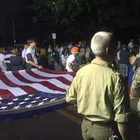 <p>Soldiers and civilians hold the American flag outside of the Howland Memorial Grove.</p>