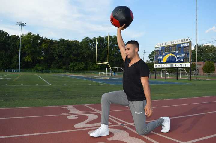 Fitness trainer Kevin Saenz holds a medicine ball above his head as he performs walking lunges down the Hackensack High School track.