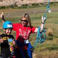 <p>Ingrid Milne celebrates with a camper after a successful zipline run at a SeriousFun camp in Colorado.</p>