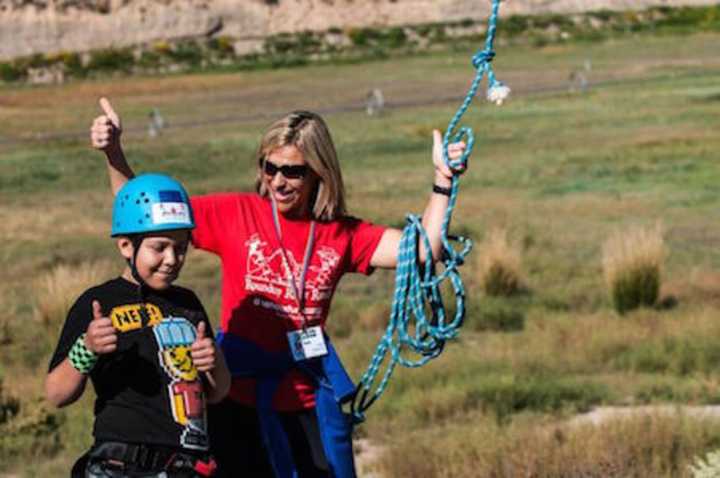 Ingrid Milne celebrates with a camper after a successful zipline run at a SeriousFun camp in Colorado.