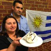 <p>Sandra Salazar holds a chaja cake, a traditional Uruguayan pastry, while her husband Omar Gomez looks. The Uruguayan flag is in the background. The couple have opened Capri&#x27;s Cuisine, specializing in Uruguayan pastries, in Norwalk.</p>