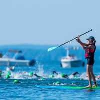 <p>A woman on a paddleboard keeps an eye on the swimmers near the start of the event.</p>