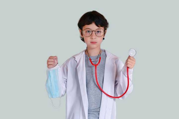 A boy dressed as doctor holding a mask.