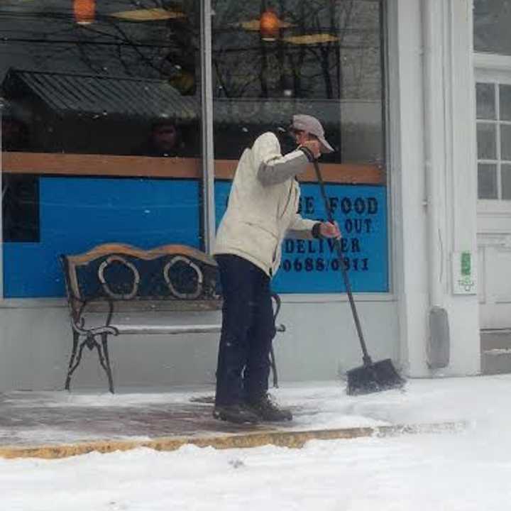 A man sweeps snow from the sidewalk in front of the Beijing Restaurant in downtown Darien during Saturday&#x27;s storm. 