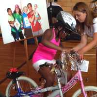 <p>Lucia Villani helps Grace Bennett onto her new pink bike at the White Plains YMCA Wednesday. </p>