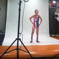 <p>Myles Griffin stands in front of cameras in front in his wrestling singlet.</p>