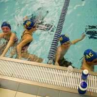 <p>Team members hang out on the edge of the pool at practice. </p>