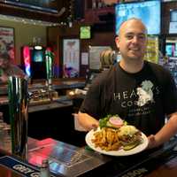 <p>Owner Ryan Healy of Healy&#x27;s Corner serves up one of his Bog Boy Burgers. The 10-ounce patty is topped with three cheeses, bacon, caramelized onions, and coleslaw.</p>