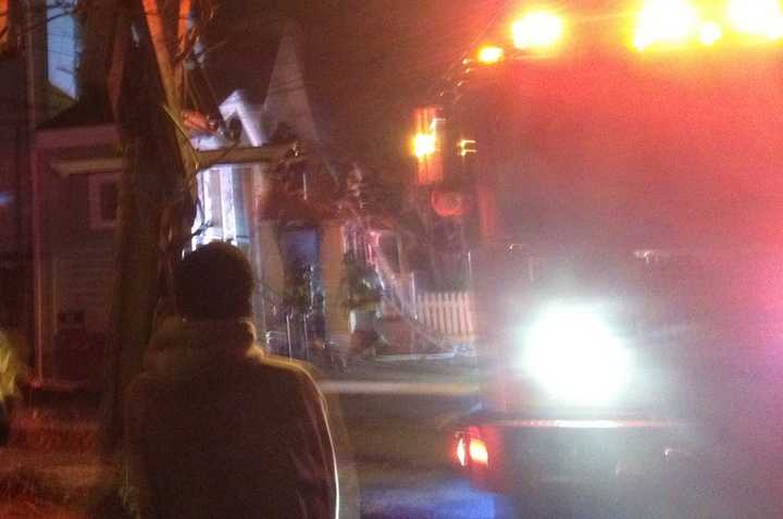 A neighbor watches as Norwalk firefighters battle to knock down the flames to enter the burning house early Saturday. 