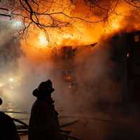 <p>Flames silhouette a firefighter as they battle a blaze at 730 Hopmeadow St. in Simbury on Saturday, Dec. 14. </p>