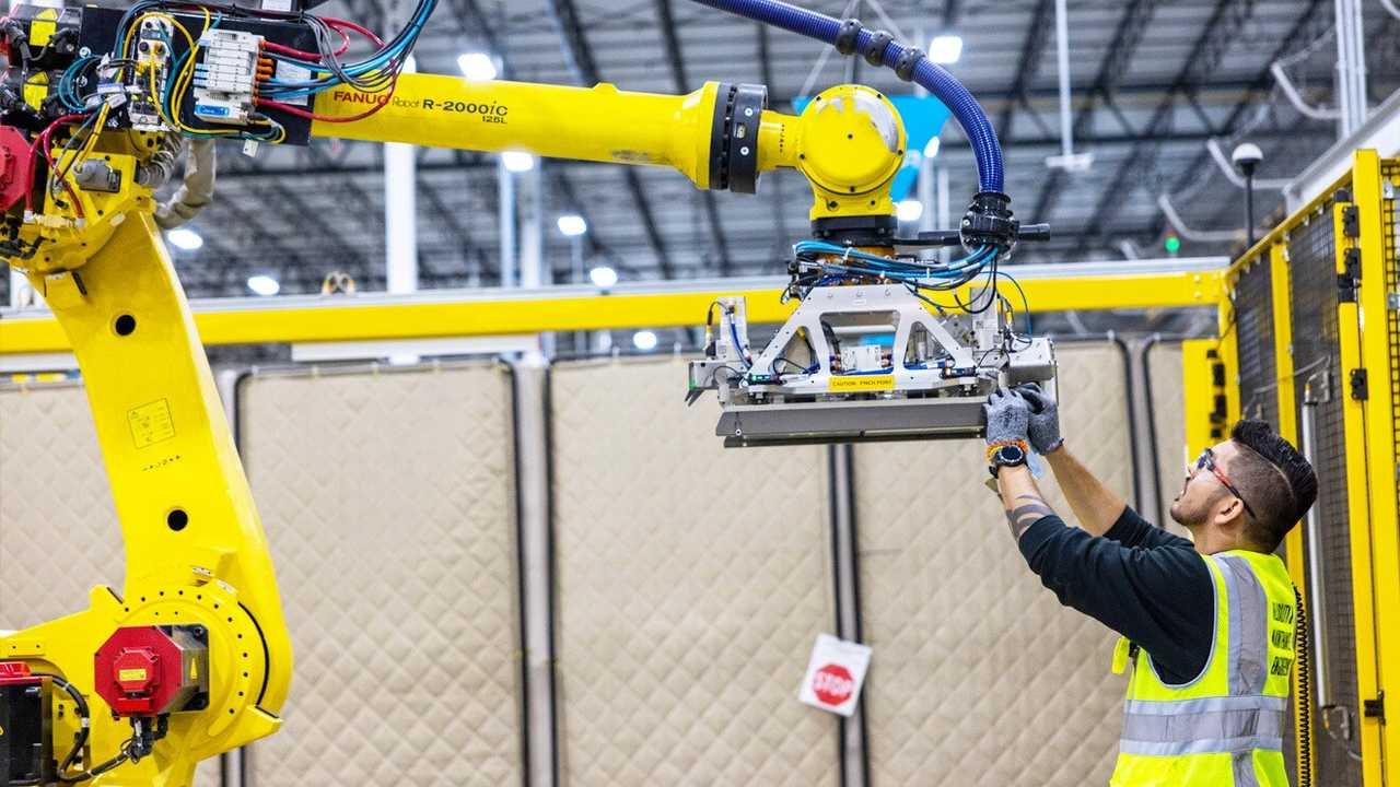 An Amazon employee working on a robotic arm in a warehouse.