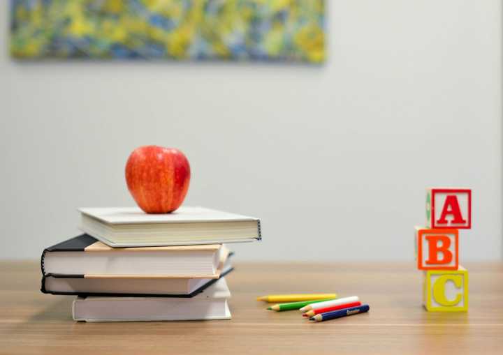An apple stacked on top of books, next to colored pencils and letter blocks.