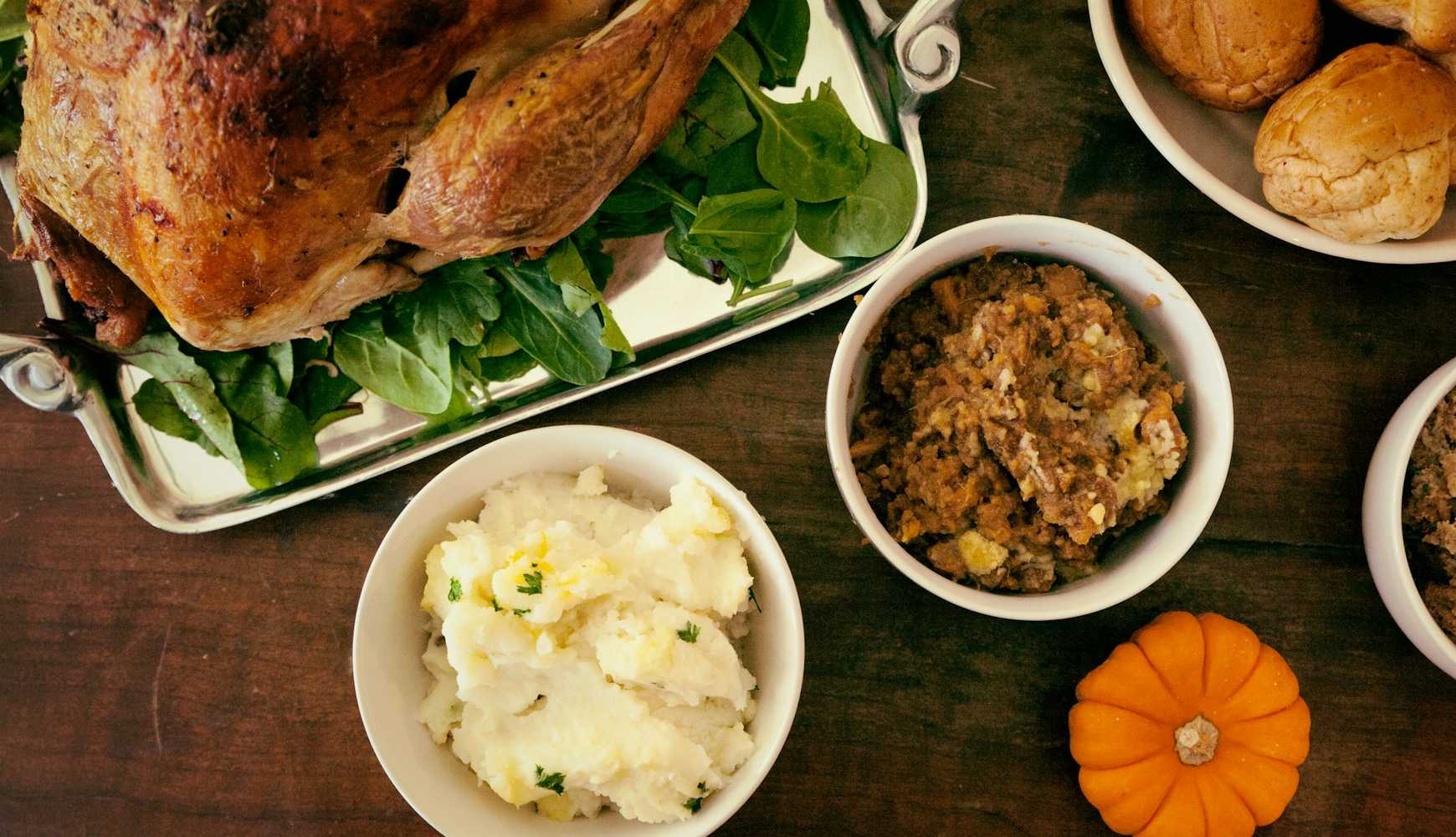 
Turkey, stuffing, mashed potatoes, and bread rolls on a Thanksgiving dinner table.
