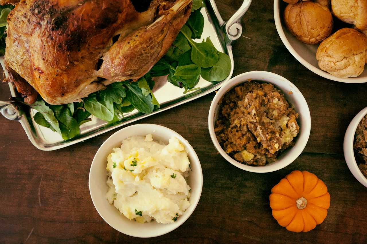 Turkey, stuffing, mashed potatoes, and bread rolls on a Thanksgiving dinner table.
