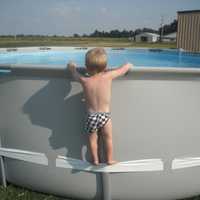 <p>A young child using a compression strap to stand on the side of an above-ground pool that was recalled in July 2025.</p>